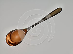Large silver tablespoon holding a brown egg on white background