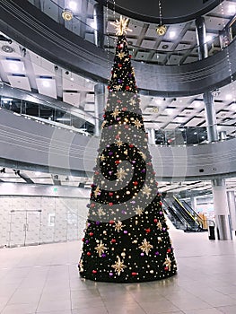 a large slender festive decorated Christmas tree stands in a spacious room