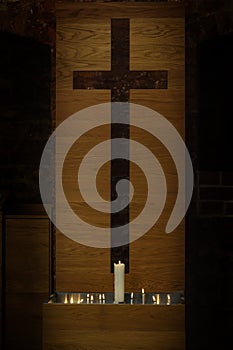 Large and small burning candles in front of a modern simple cross cut out of a wooden plate in the historic St. Georgen church in