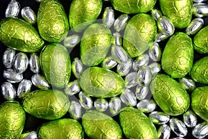 Large & small green, lime green and silver spring colours of foil wrapped chocolate easter eggs, against a black background.