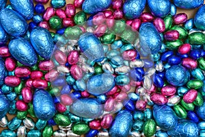 Large & small pink, blue, green and silver foil wrapped chocolate easter eggs, against a pale background.