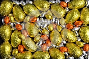 Large & small yellow, gold, orange and silver spring colours of foil wrapped chocolate easter eggs, against a black background