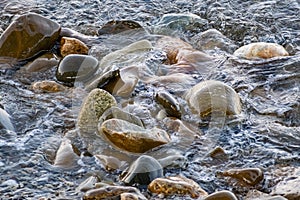 Large and smooth stones in the coastal waves of salty sea water. The coast of the black sea foams and roars