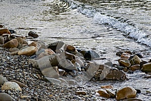 Large and smooth stones in the coastal waves of salty sea water. The coast of the black sea foams and roars