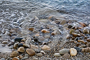 Large and smooth stones in the coastal waves of salty sea water. The coast of the black sea foams and roars, beating against a hug