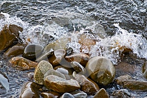 Large and smooth stones in the coastal waves of salty sea water. The coast of the black sea foams and roars, beating against a hug