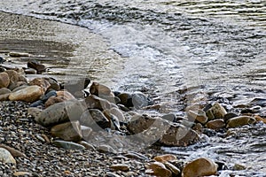 Large and smooth stones in the coastal waves of salty sea water. The coast of the black sea foams and roars, beating against a hug