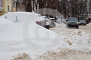 A large snowdrift against the backdrop of a city street with cars.