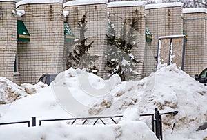 A large snowdrift against the background of a wall of a brick building.