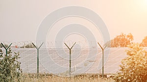 Large solar station with blue photovoltaic panels fenced with lattice and barbed wire. Producing clean energy from the