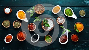 Large spice and herb collection in bowls and spoons. Indian spices. On a black wooden background.