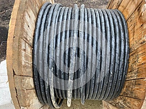 Large spool with black thick electrical wire or cable. Wooden coil with electrical industrial wires at a construction site