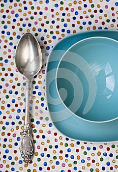 A large spoon rests on tablecloth next to two blue plates