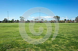 A large sports ground with green grass with many suburban residential houses in the distance. Background texture of a public park