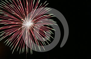 Large starburst firework with white center transitioning to red then to green in the black sky on the Fourth of July