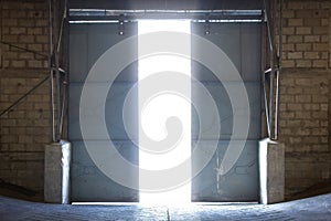 Large steel door inside an old warehouse opens into an external light.