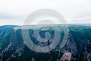 Large steep cliffs and plateau under overcast sky and fog