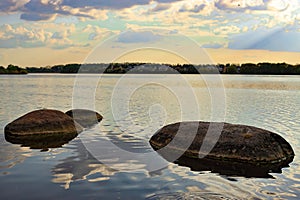 Large stones in the lake, clouds are reflected in the water, at sunset