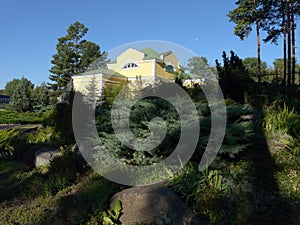 Large stones in a park lying among green lush bushes on the background of a house standing behind a fence of iron bars.