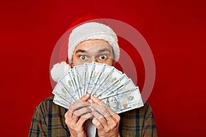 large studio portrait of young man in Christmas hat with wad of money in his hands holding fan of dollars in front of