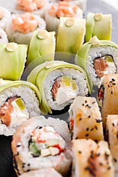 Large sushi set of various sushi rolls is served on black square metal slate.