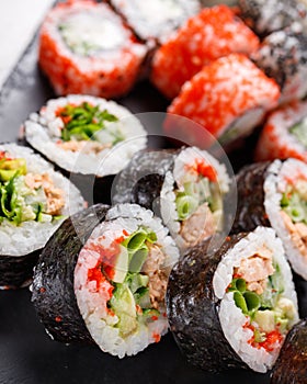 Large sushi set of various sushi rolls is served on black square metal slate.