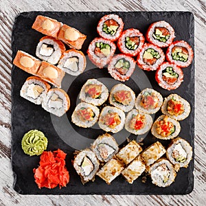 Large sushi set of various sushi rolls is served on black square metal slate.