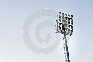 Large tall high outdoor stadium spotlights on rigid frame construction under natural sunlight.