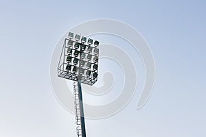 large tall high outdoor stadium spotlights on rigid frame construction under natural sunlight.