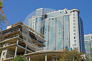 A large tall house with glass walls and an unfinished building with a tower crane