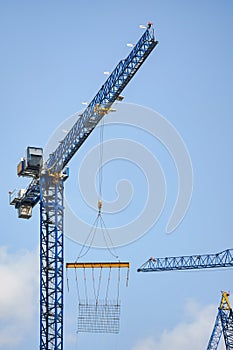 Large tall industrial crane at skyscraper building site, steel bars grid hanging under when moved, clear sky background