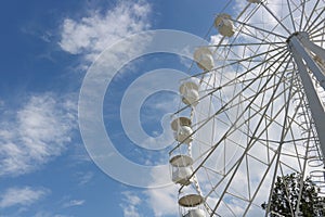 A large, tall white Ferris wheel against a blue sky background. Happy feelings from the summer holidays