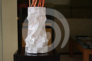 A large tall white vase printed with a 3d printer stands on a table