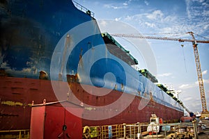 A large tanker cargo ship is being renovated and painted in shipyard dry dock