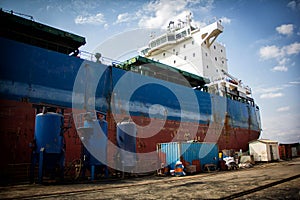 A large tanker cargo ship is being renovated and painted in shipyard dry dock