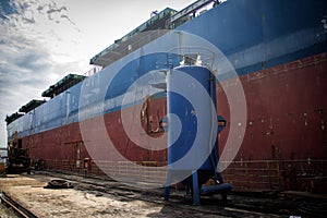 A large tanker cargo ship is being renovated and painted in shipyard dry dock