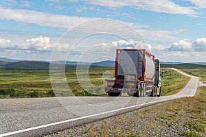 Large tanker truck on the road on a background of a green meadow and clouds