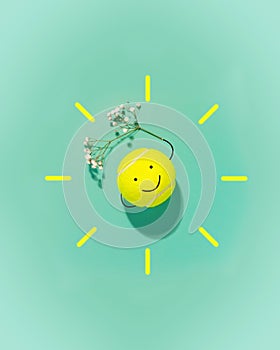 Large tennis ball in the form of a smiley face and flower on blue background