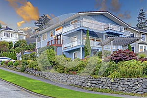 Large three story tall blue house with summer landscape and rock wall.