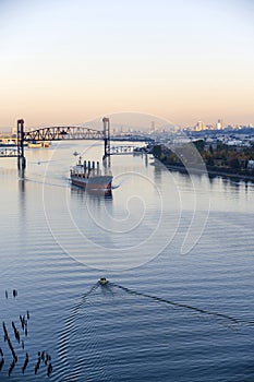 Large-tonnage riverboat cargo ship sails under raised bridge along the Willamette River in the background of Portland down town