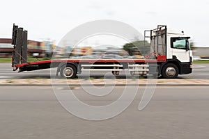 Large tow truck with a white cab and a red platform. Motion blur