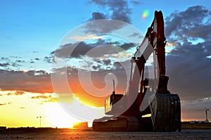 Large tracked excavator on a construction site against the background of the awesome sunset. Road repair, asphalt replacement.