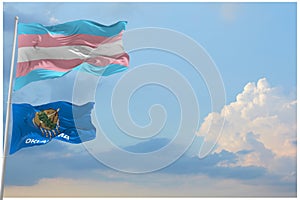 large Transgender Pride flag and flag of Oklahoma state, USA waving in wind at cloudy sky. Freedom and love concept. Pride month.