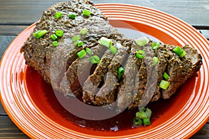 Large tri-tip church of beef just off the grill cooked medium well on a red plate with green onion garnish in its own juice on the photo