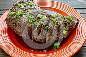 Large tri-tip church of beef just off the grill cooked medium well on a red plate with green onion garnish in its own juice on the photo