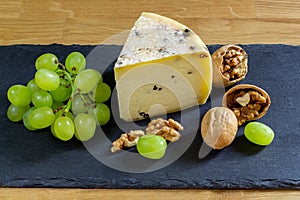 Large triangle of cheese with spices, grapes and walnuts. Russian farm hard aged cheese