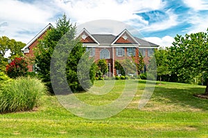 Large, two-story, brick country house with trees and an expansive lawn in the front yard