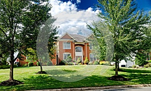 Large, two-story, brick country house with trees and an expansive lawn in the front yard