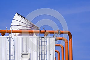 Ventilation chimney with pipelines and exhausting machine system on factory building roof against blue sky