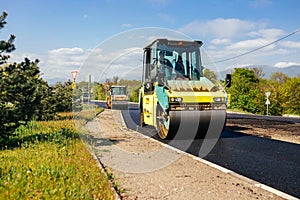 Large vibratory roller compact fresh asphalt on the road surface of a new construction site